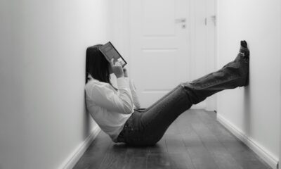 Imagem preto e branco de uma mulher frustrada sentada no chão com um livro sobre a face.