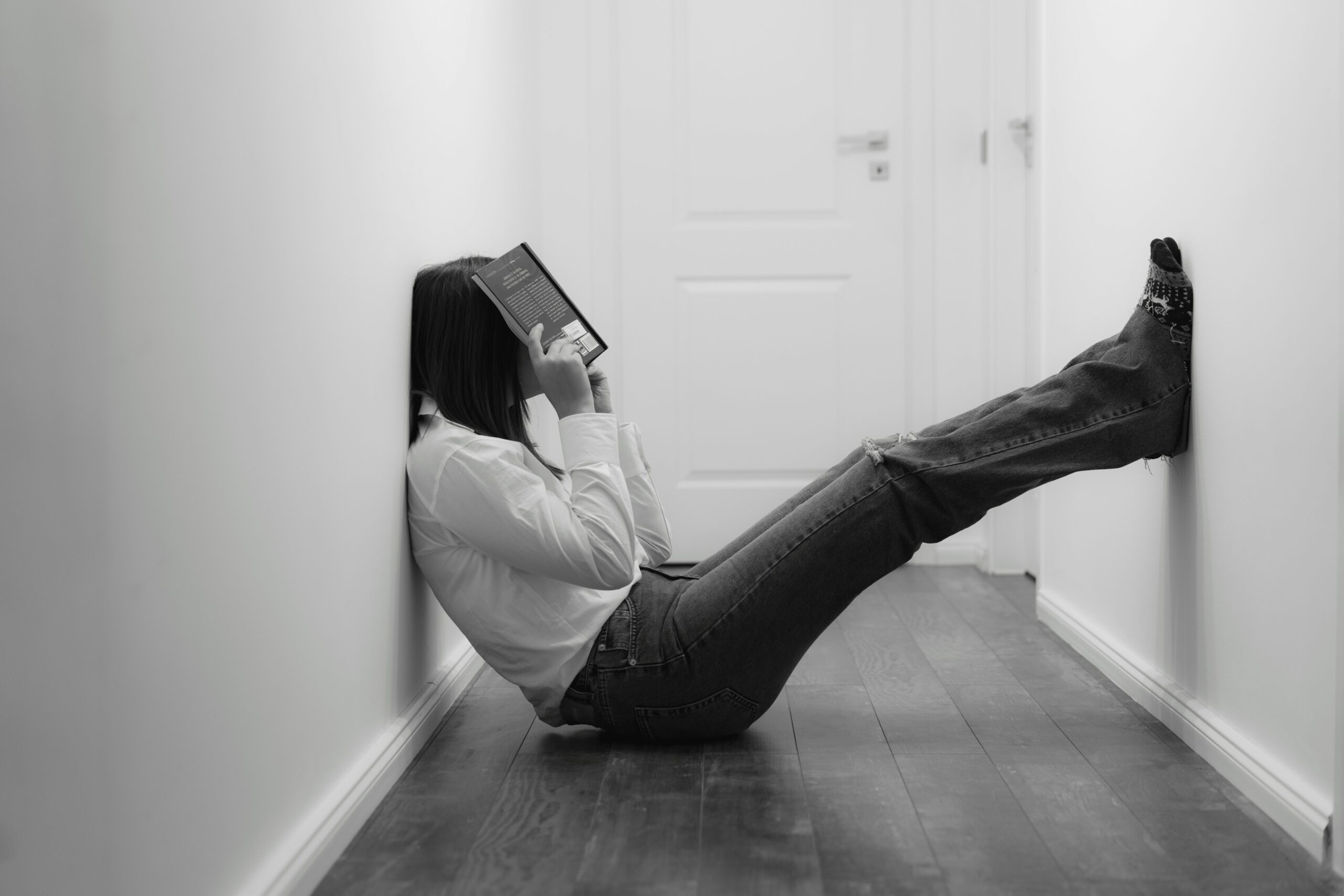 Imagem preto e branco de uma mulher frustrada sentada no chão com um livro sobre a face.